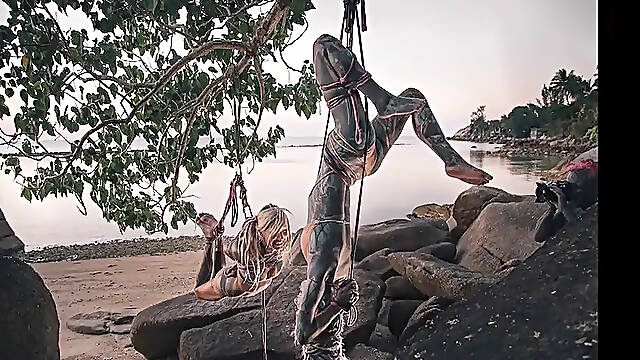 Tattooed babe suspended in Shibari bondage on Thai beach